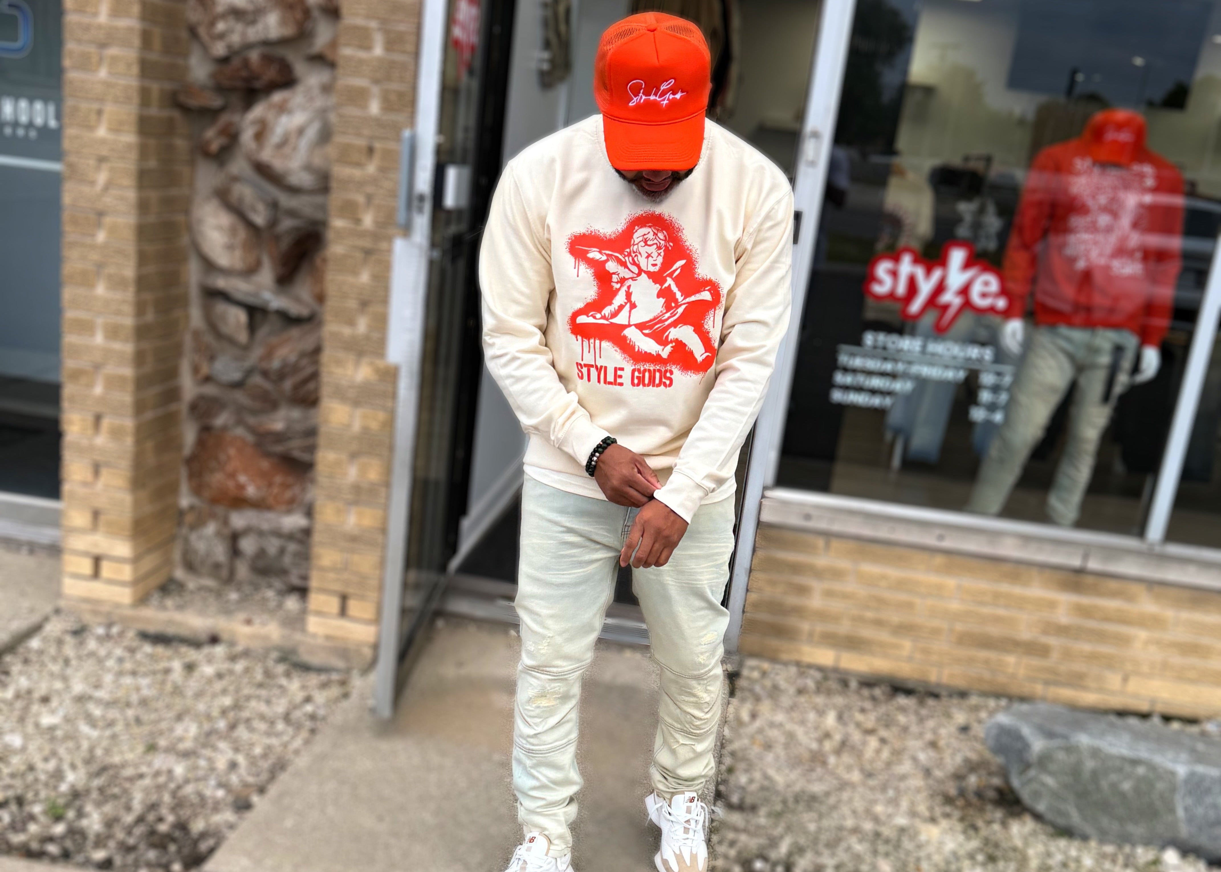 Person wearing a white sweatshirt and pants with a orange logo, standing outside a store.